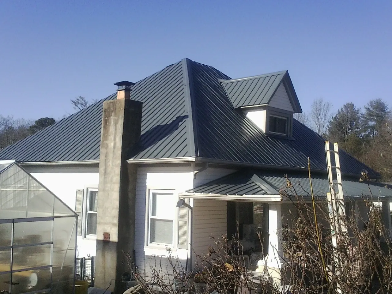 Dark blue standing seam metal roof on a white farmhouse with dormer — Slate & Tile Roof Repair by Roofing Brothers in West End