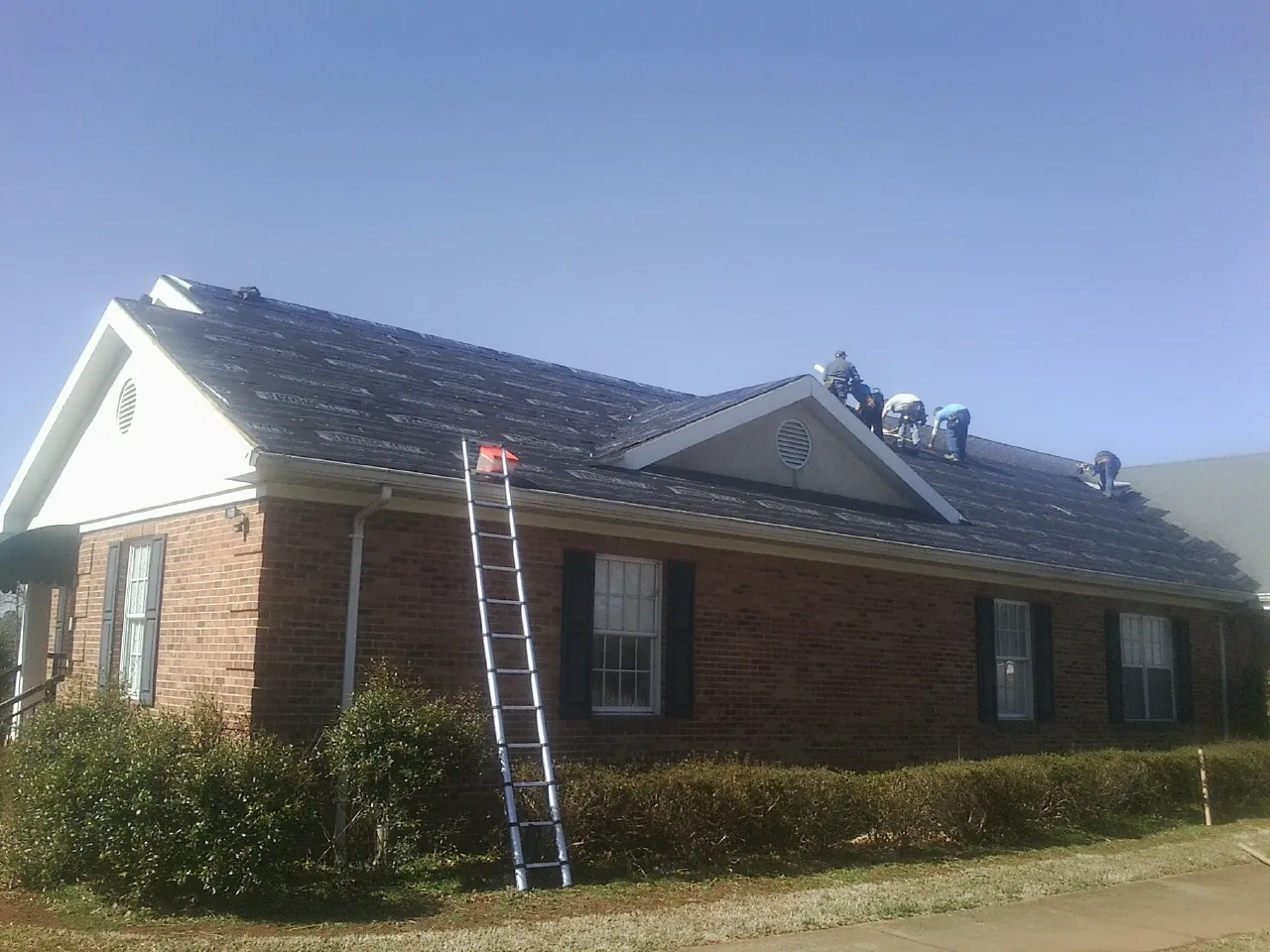 Crew tearing shingles off a brick ranch roof with a ladder set — Emergency Roof Repair work by our crew in West End