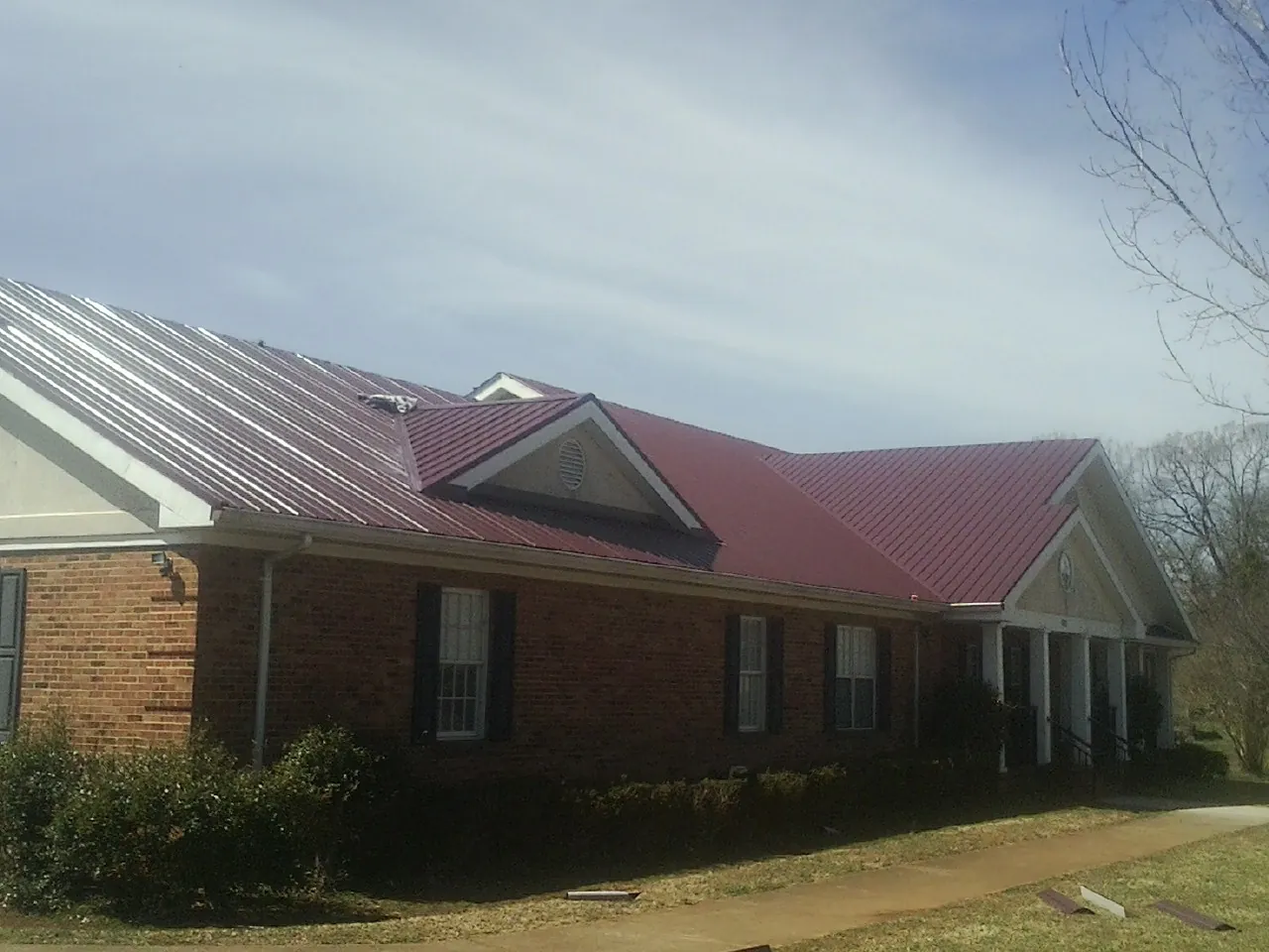 Red metal roof with gabled entries on a long brick building, from a Hail Damage Roof Repair job in West End