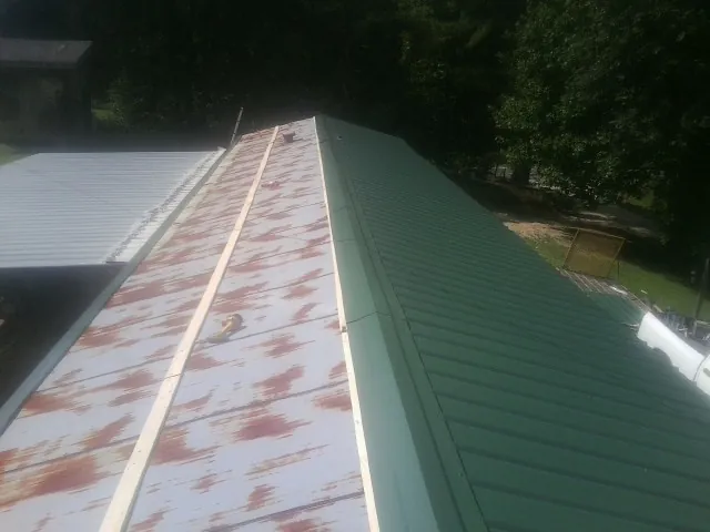 Old rusted panels beside newly installed green metal roofing — Wind Damage Roof Repair by Roofing Brothers in West End