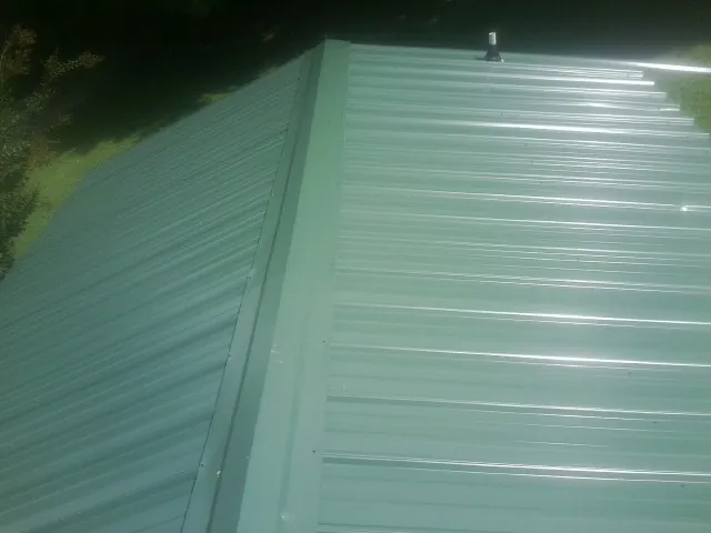 New green metal panels meeting at the ridge of a roof — Flat Roof Repair work by our crew in West End