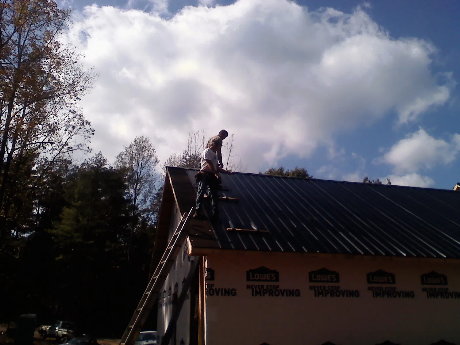 Roofer fastening dark metal panels high against a cloudy sky, from a Roof Inspection job in West End