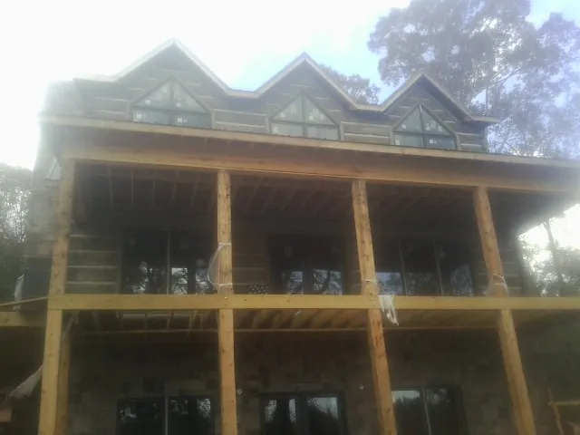 Dormers and porch framing on a large log home under construction — Roof Coating work by our crew in West End