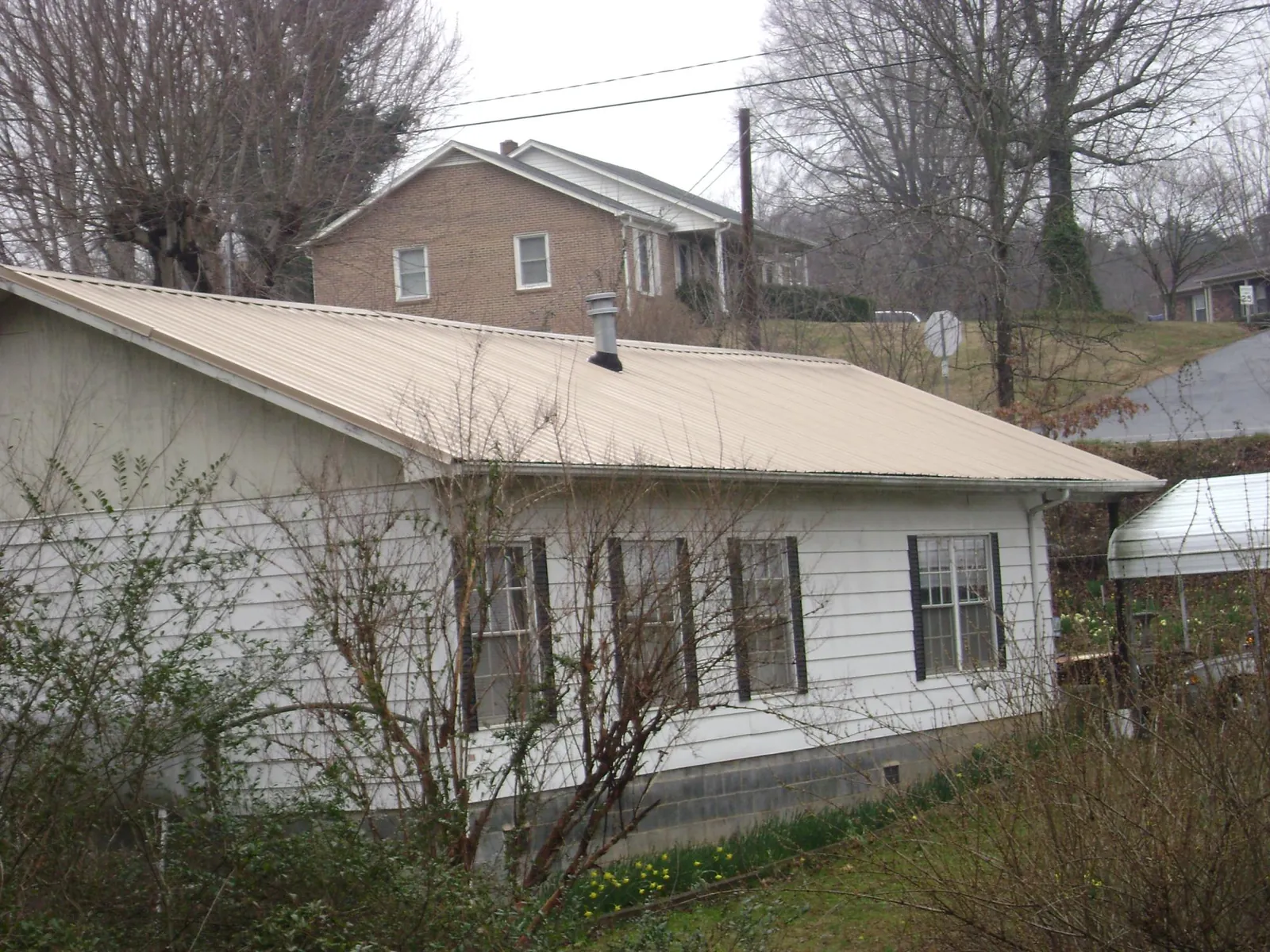 Tan metal roof on a white sided house set into a hillside — Commercial Roofing by Roofing Brothers in West End