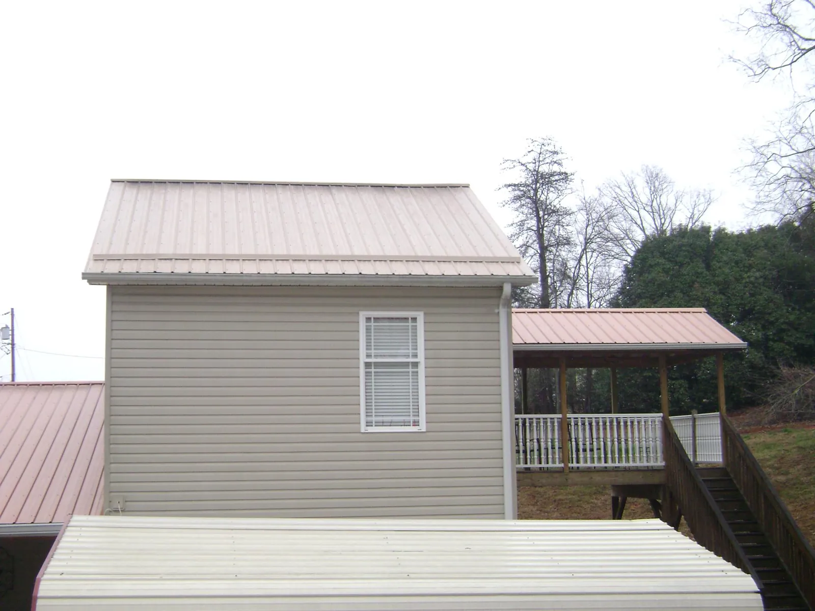 Tan metal roofs on a two story addition and attached porch, from a Roof Replacement job in West End
